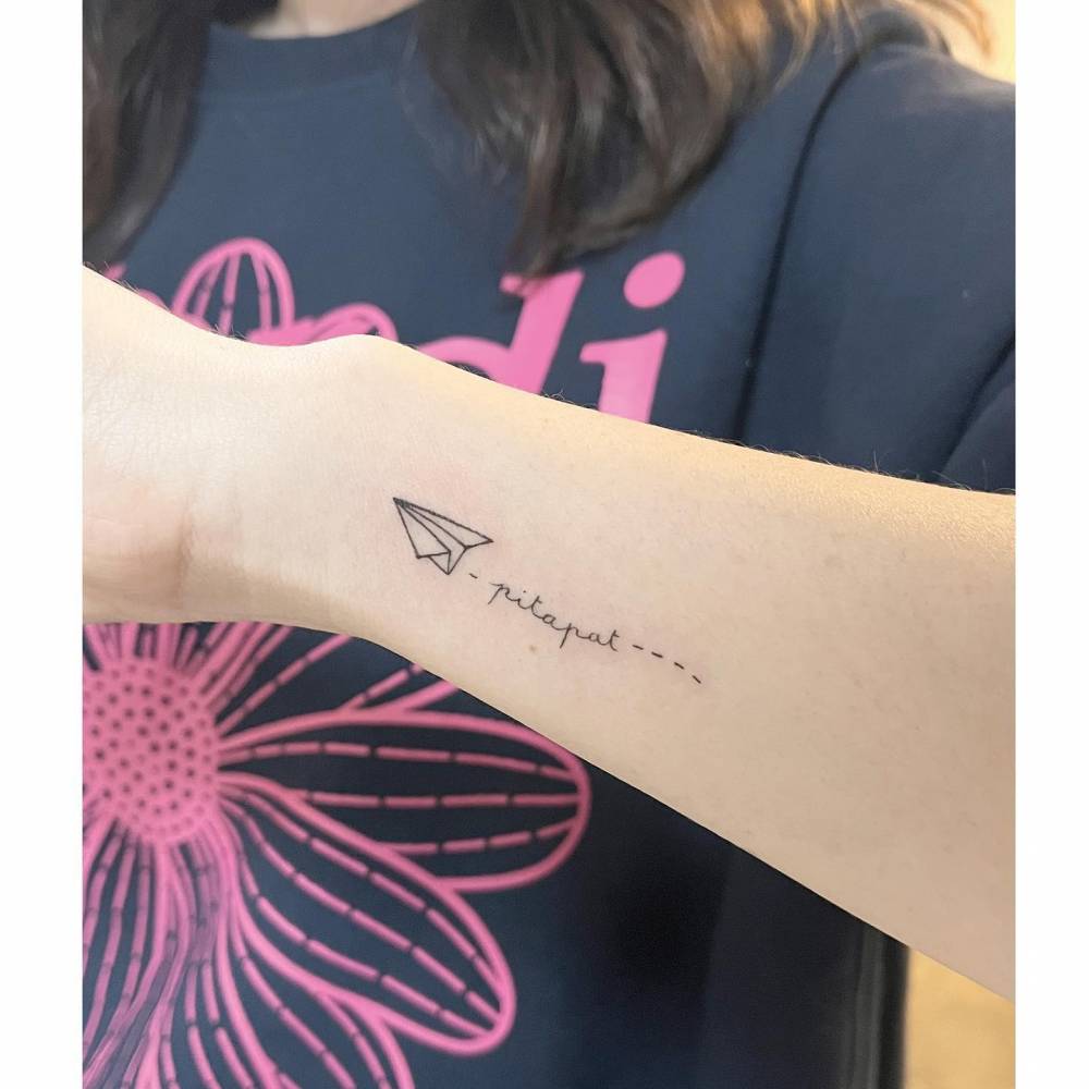 Paper plane and word "pitapat" tattooed on the wrist.