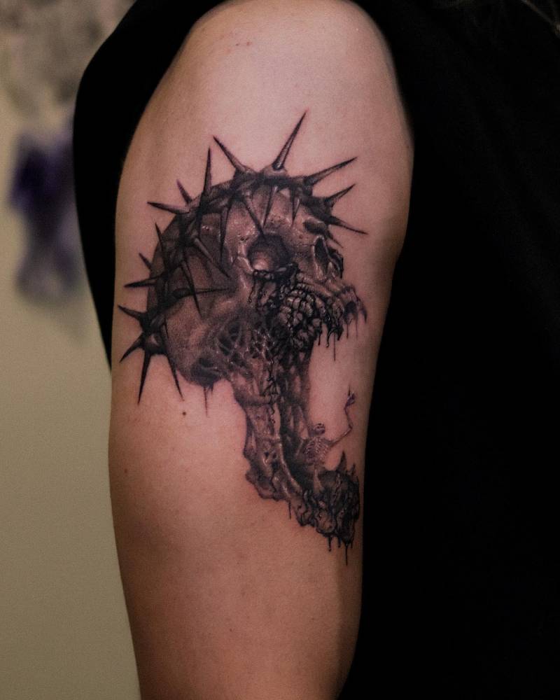 Black and grey style skull wearing a crown of thorns tattooed on the upper arm.