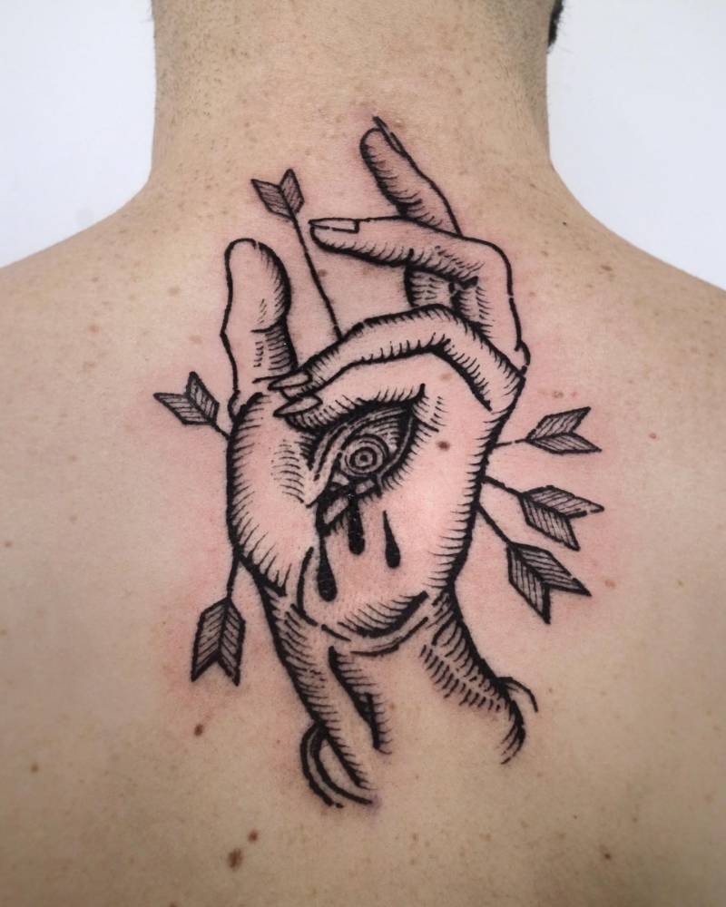 Blackwork style hand, eye and arrows tattoo located on the upper back.