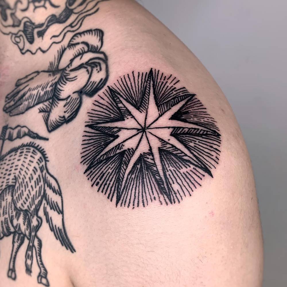 Star tattoo placed on the shoulder, done in engraving style.