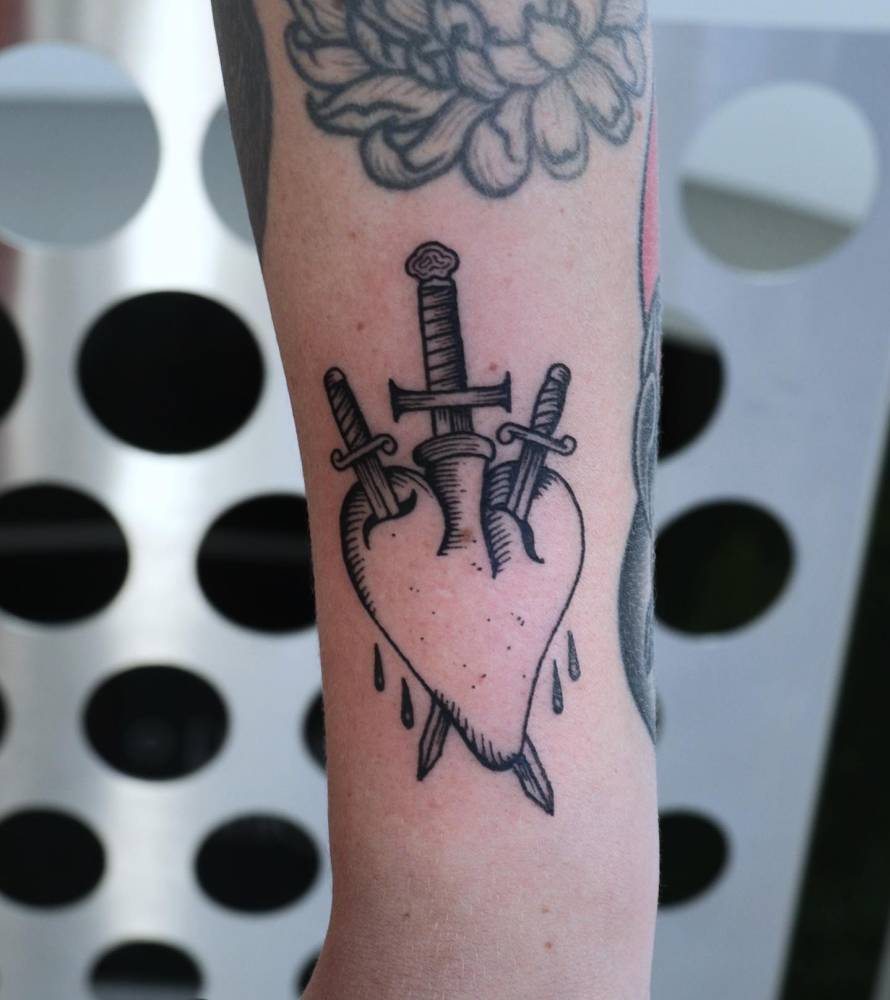 Heart and dagger tattoo located on the forearm, done in engraving style.