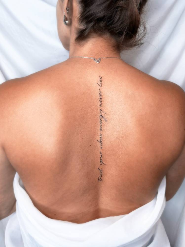 "Trust your vibes, energy never lies" lettering tattoo handwritten on the spine.