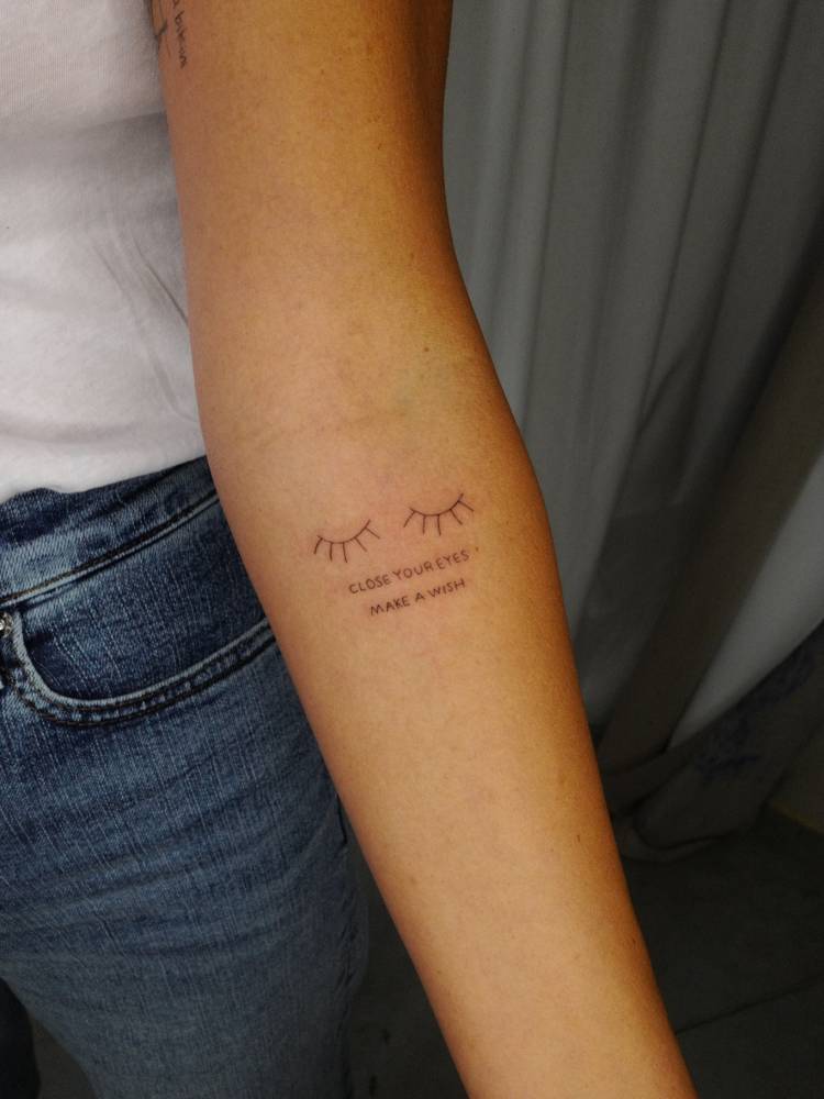 "Close your eyes, make a wish" and eyelashes tattoo located on the inner forearm.
