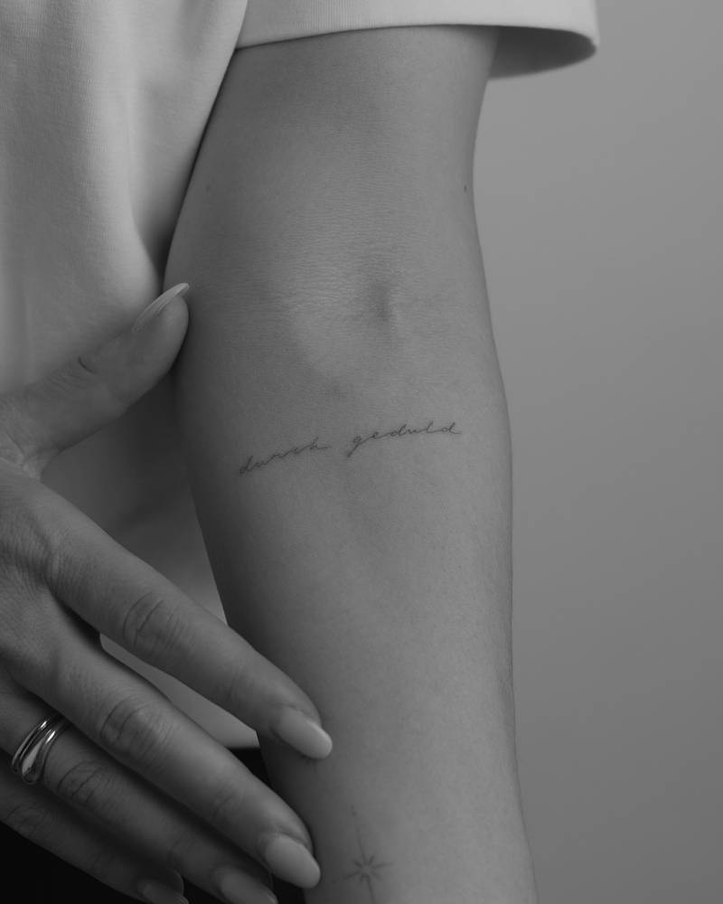 "Durch geduld" lettering tattoo in handwritten font placed on the inner forearm.