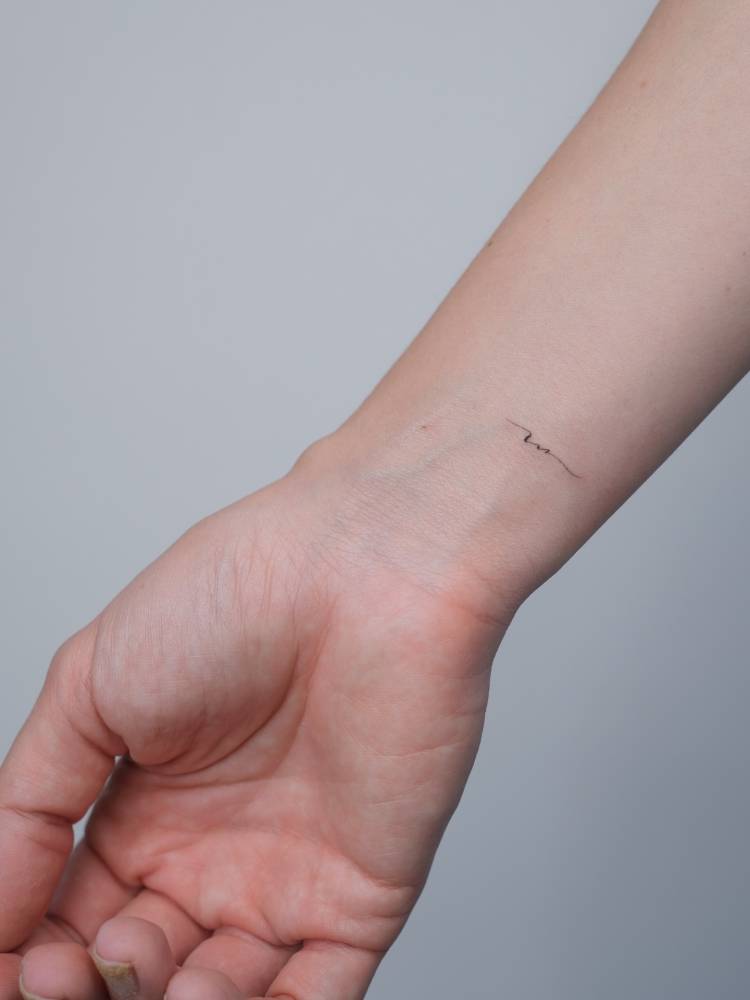 Tiny minimalistic initial tattoo located on the wrist.