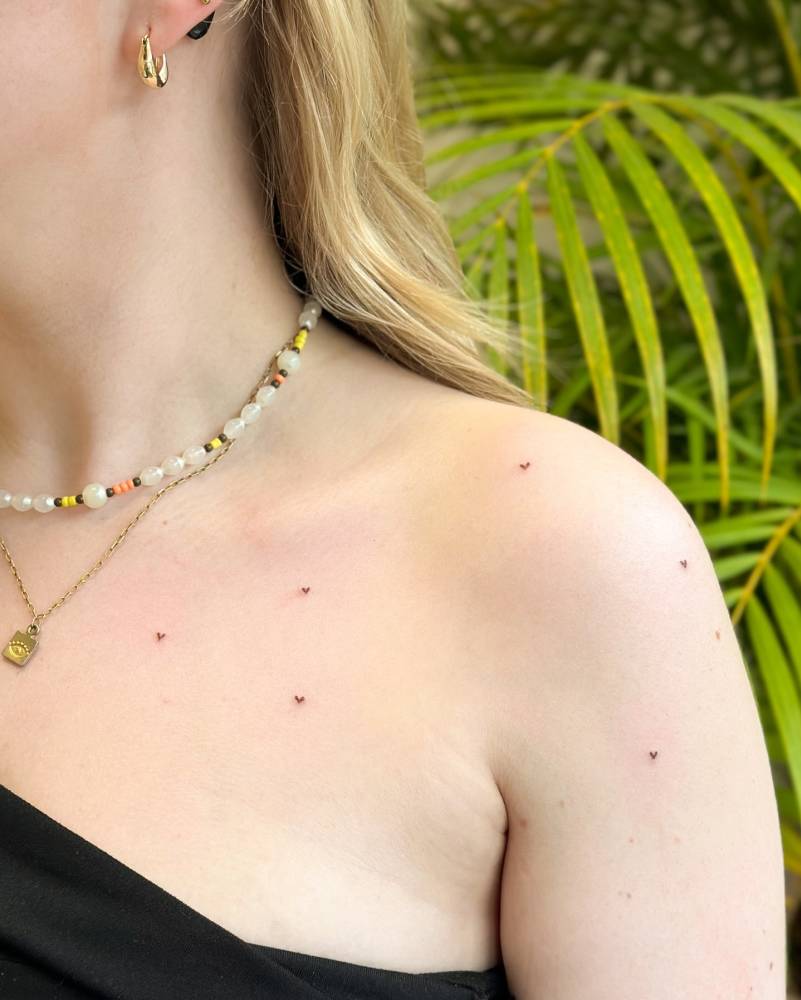 Minimalistic style heart freckles tattoo located on the chest and shoulder.