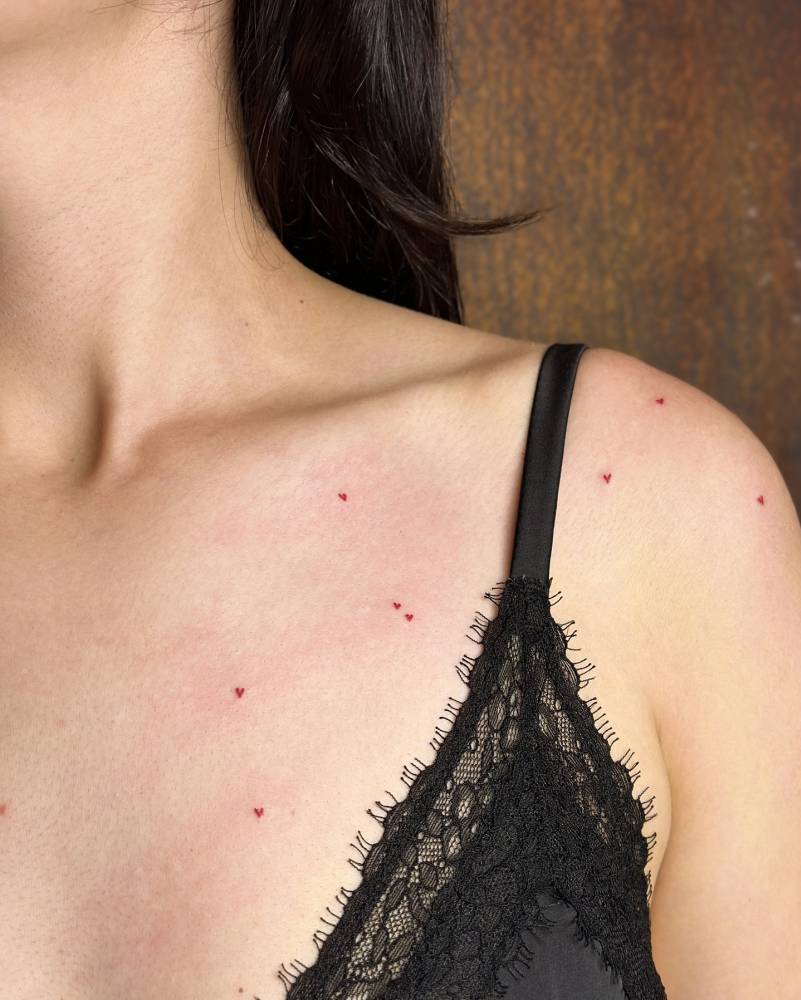 Minimalistic style heart freckles tattoo located on the chest and shoulder.
