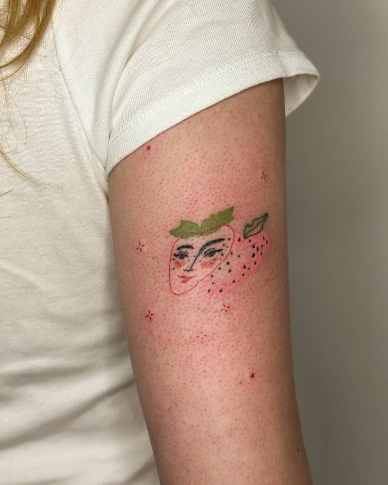 Strawberry face tattoo located on the tricep, illustrative style.