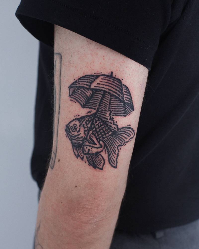 Fish holding and umbrella tattooed on the tricep, engraving style.
