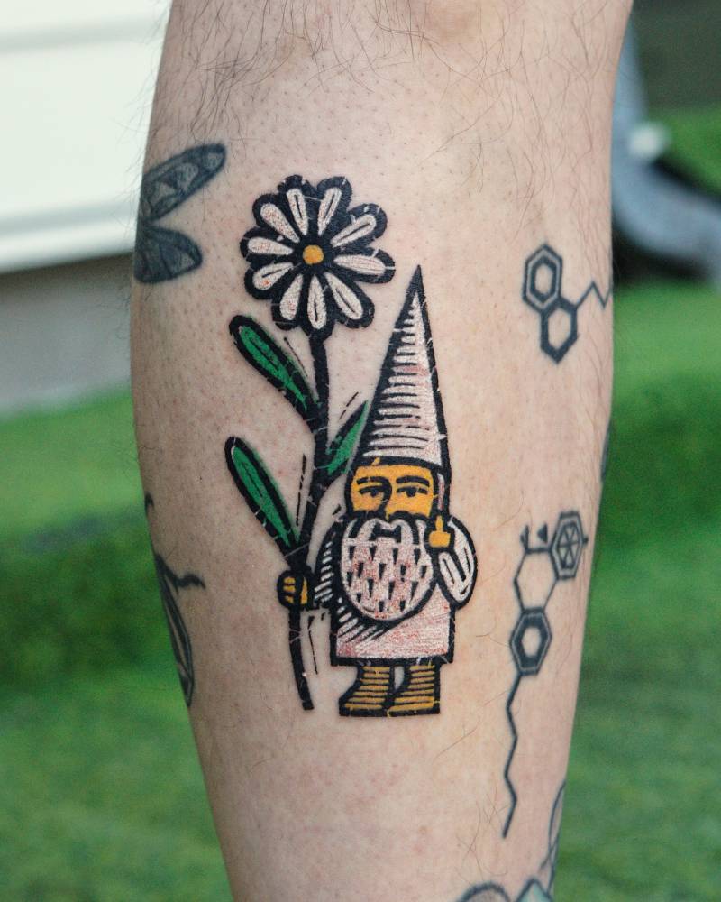 Gnome holding a daisy flower tattooed on the shin.