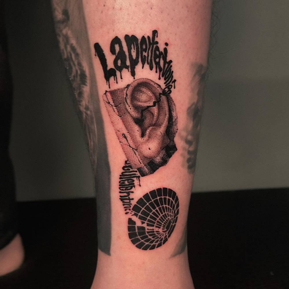 Graphic style ear tattoo located on the shin.