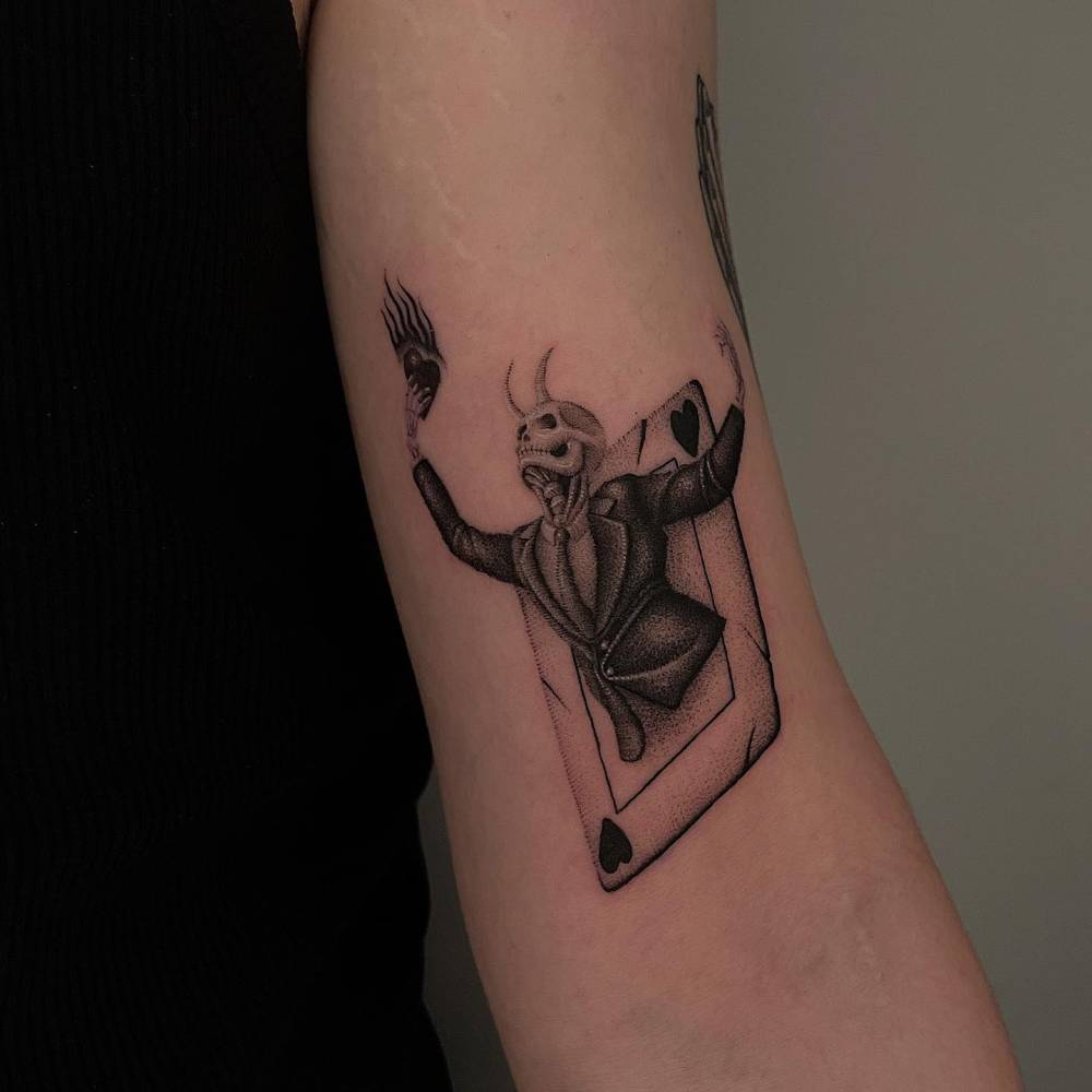 Skeleton card tattooed on the bicep, done in dotwork style.