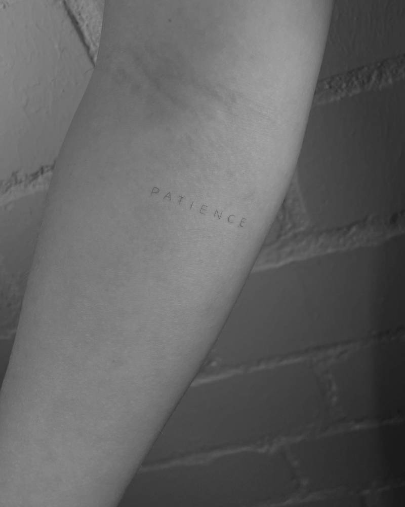 Lettering tattoo of the word "patience" done on the inner forearm.