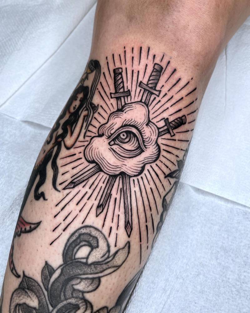 Eye cloud and swords tattoo located on the shin, done in engraving style.