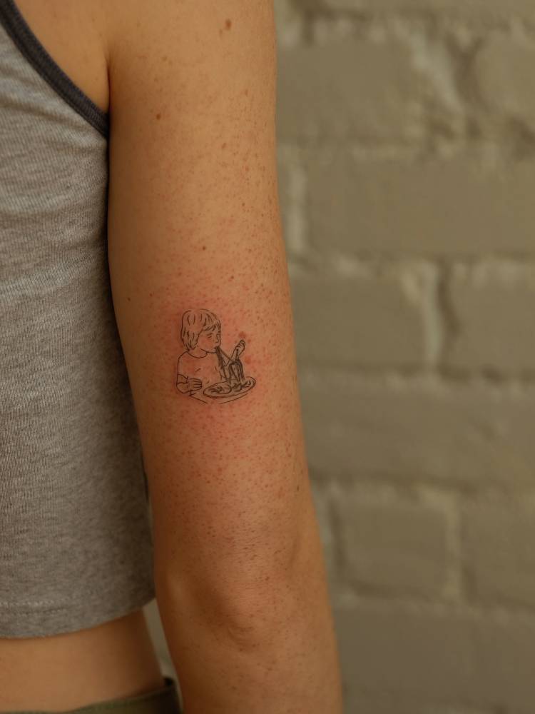 Child eating spaghetti tattooed on the tricep, fine line style.