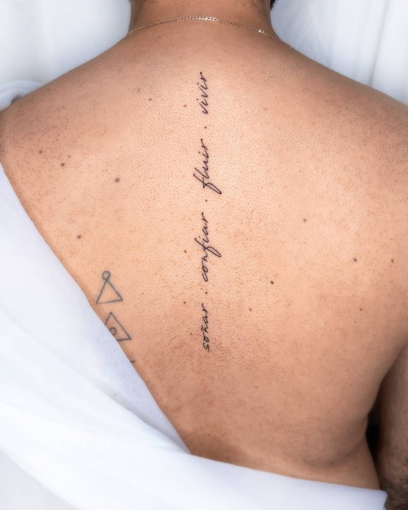 "Soñar, confiar, fluir, vivir" lettering tattoo located on the spine.