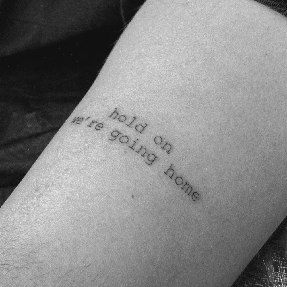 "Hold on we're going home" lettering tattoo located on the upper arm.