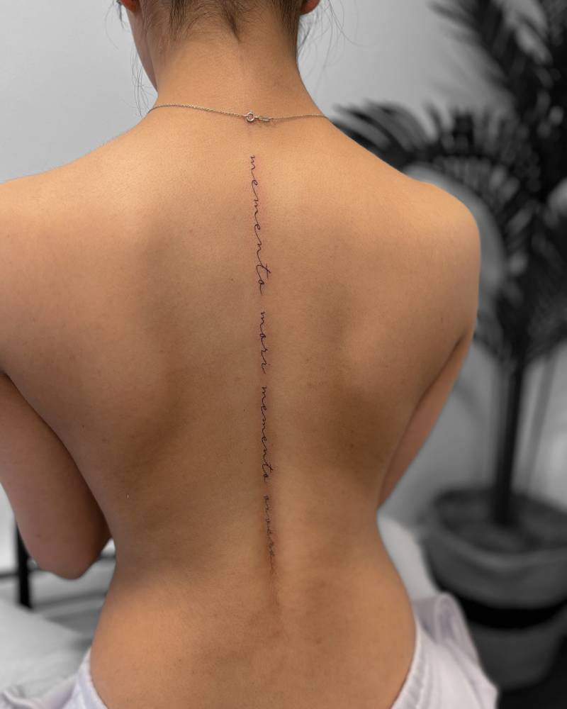 "Memento mori" and "memento vivere" lettering tattoo placed on the spine.