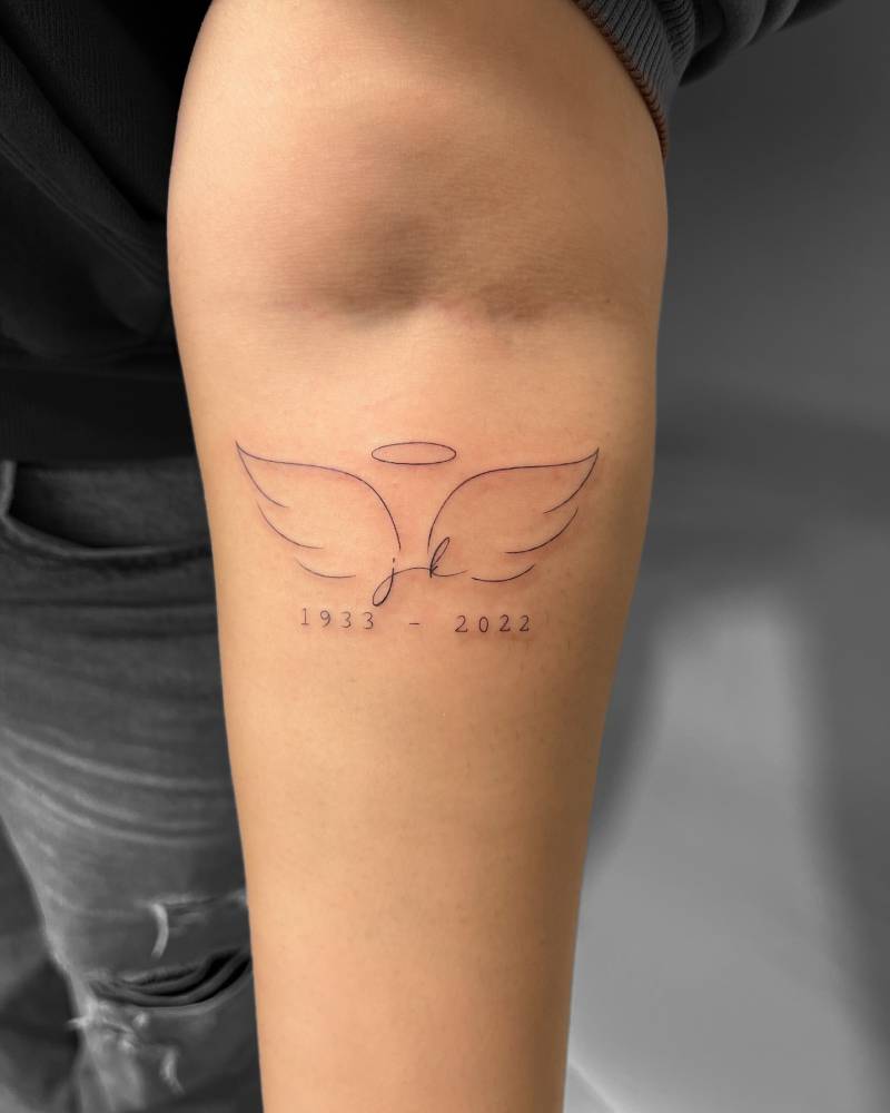 Angel wings and halo with initials tattooed on the inner forearm.