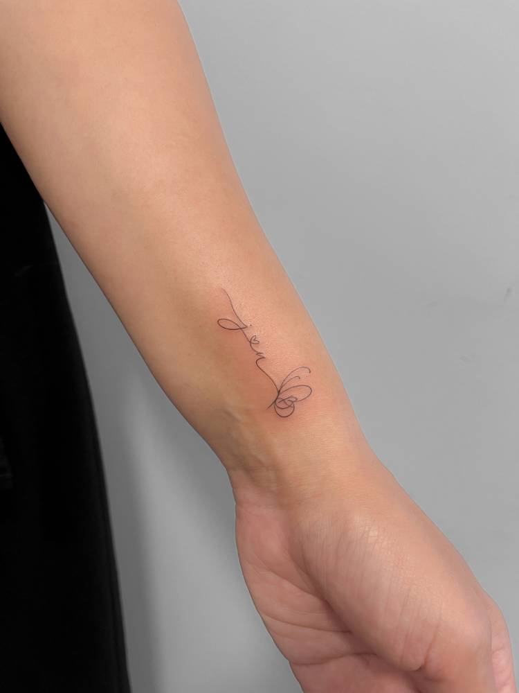 Fine line style initials and butterfly tattoo located on the wrist.