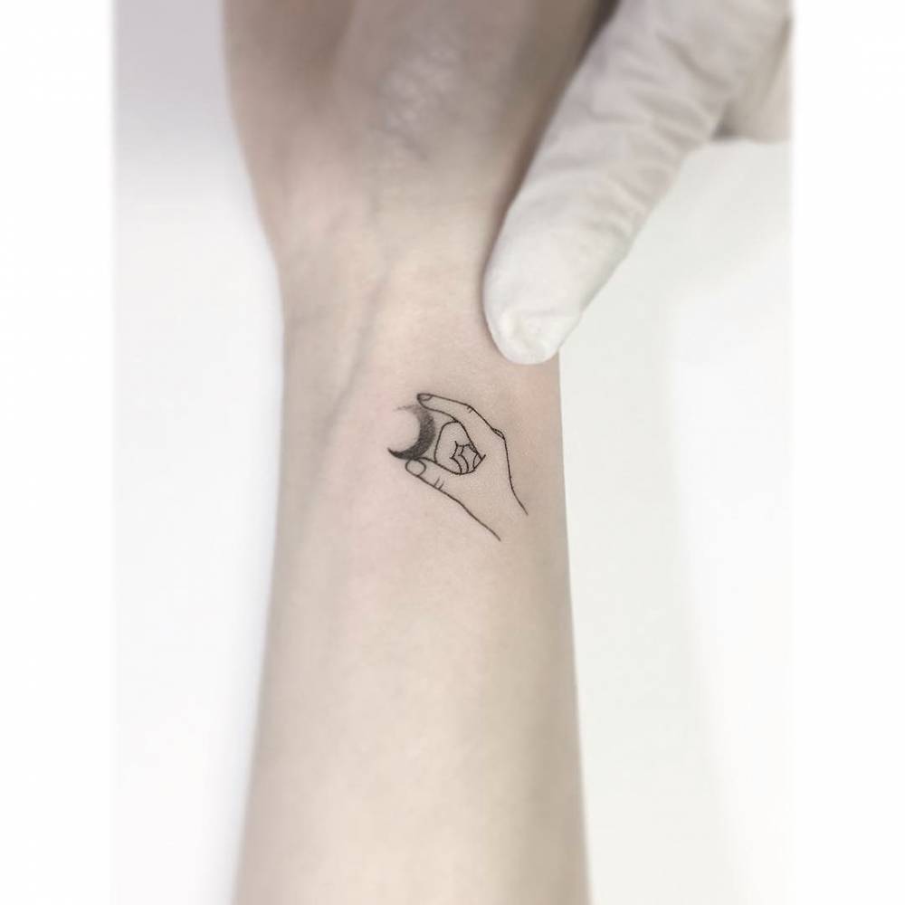 Hand hold a crescent moon tattooed on the wrist.