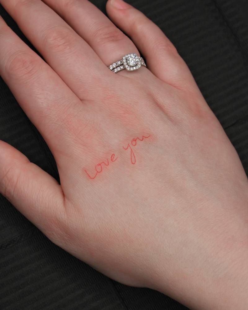 "Love you" lettering tattoo in red ink located on the hand.