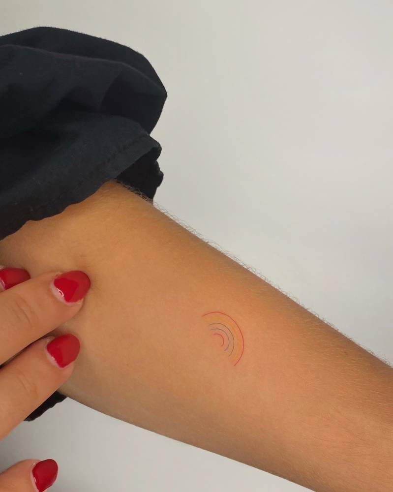 Tiny minimalistic rainbow tattoo placed on the inner forearm.