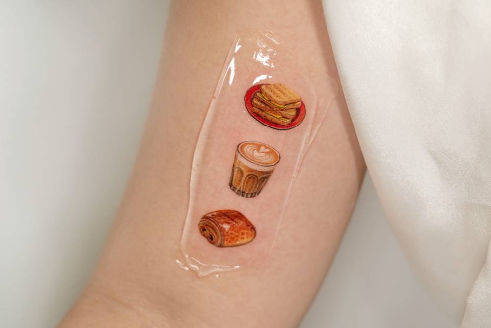 Sandwich, coffee and pain au chocolat tattoo located on the inner arm.