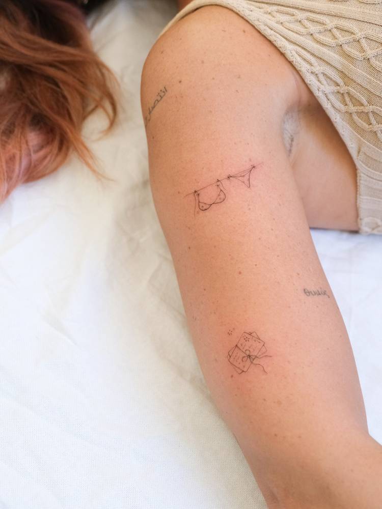 Clothes line and postcard tattoos located on the upper arm, fine line style.