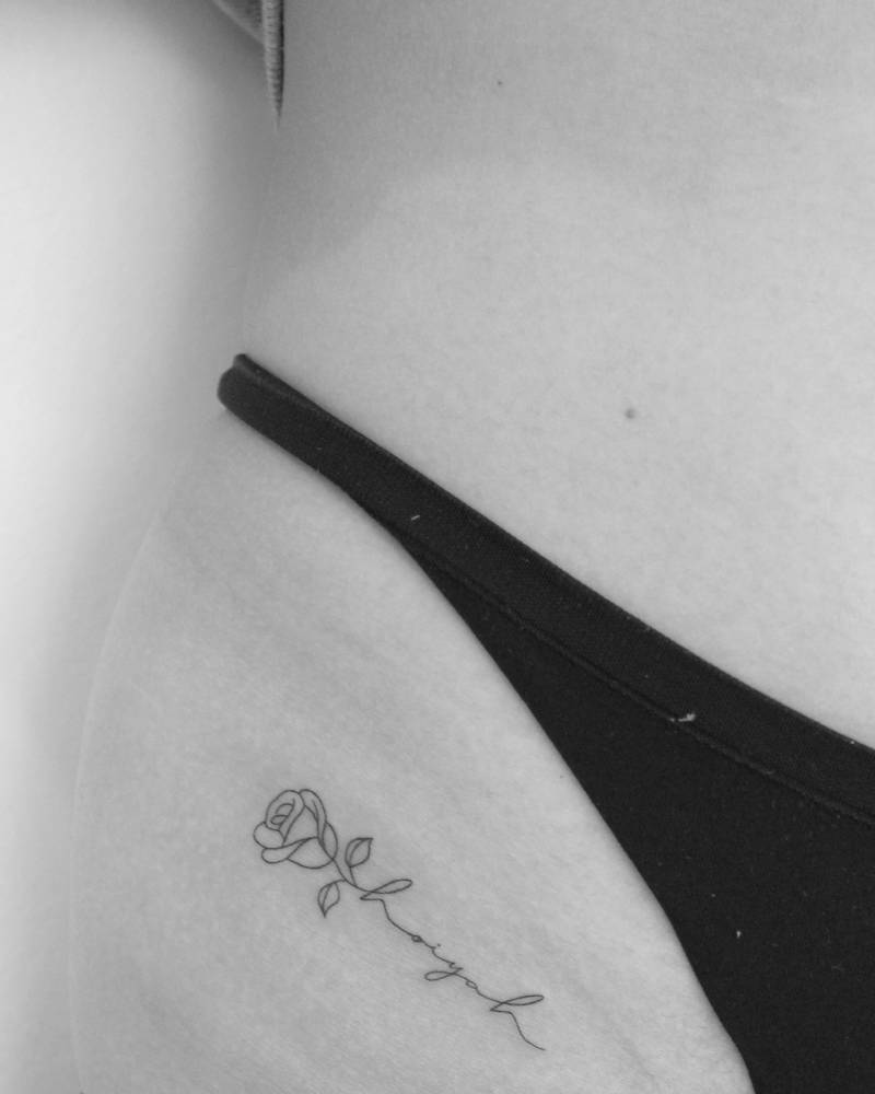 Rose and handwritten lettering tattooed on the pelvis, fine line style.