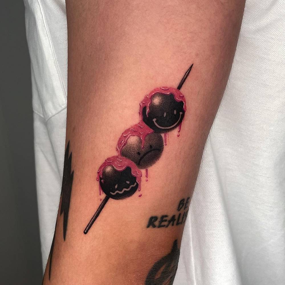 Smiley mitarashi dango tattoo in dotwork style located on the upper arm.