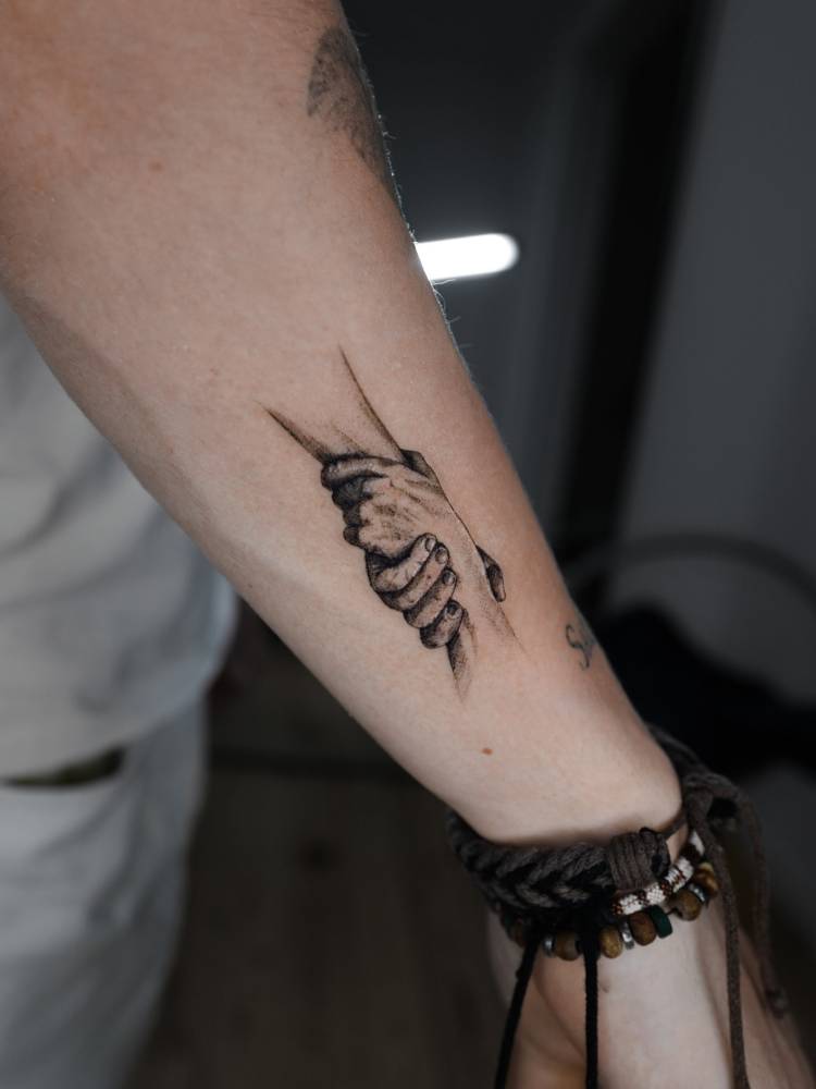 Holding hands tattoo located on the forearm, illustrative style.