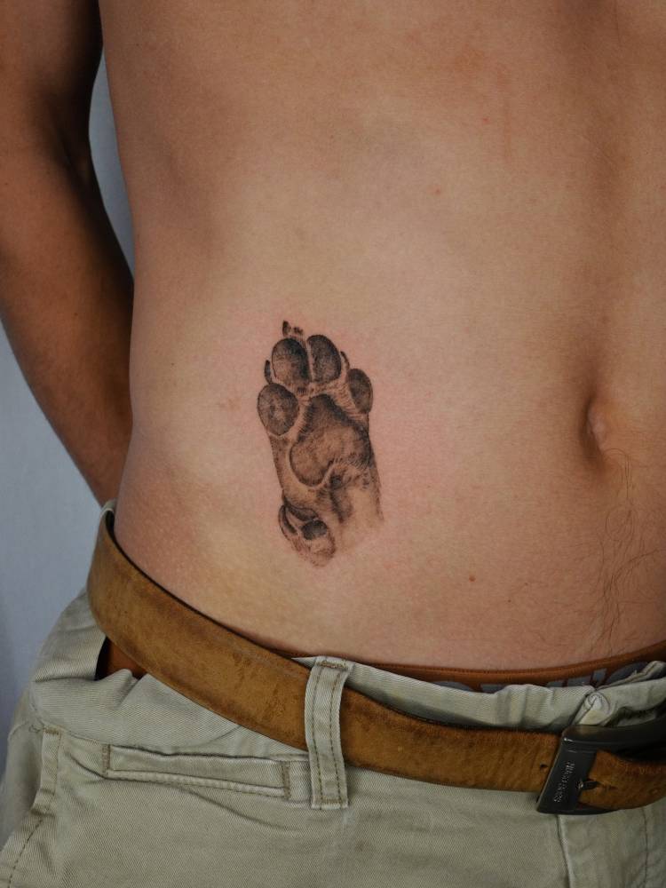 Black and grey style dog paw tattoo located on the waist.