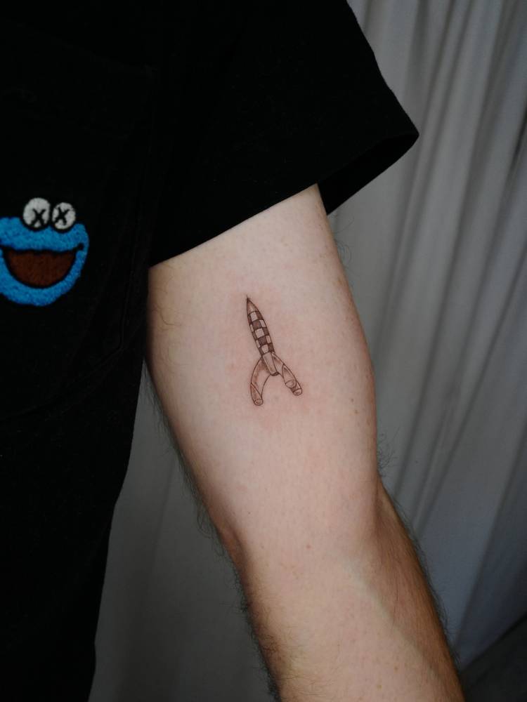 Little rocket tattoo in illustrative style located on the inner arm.