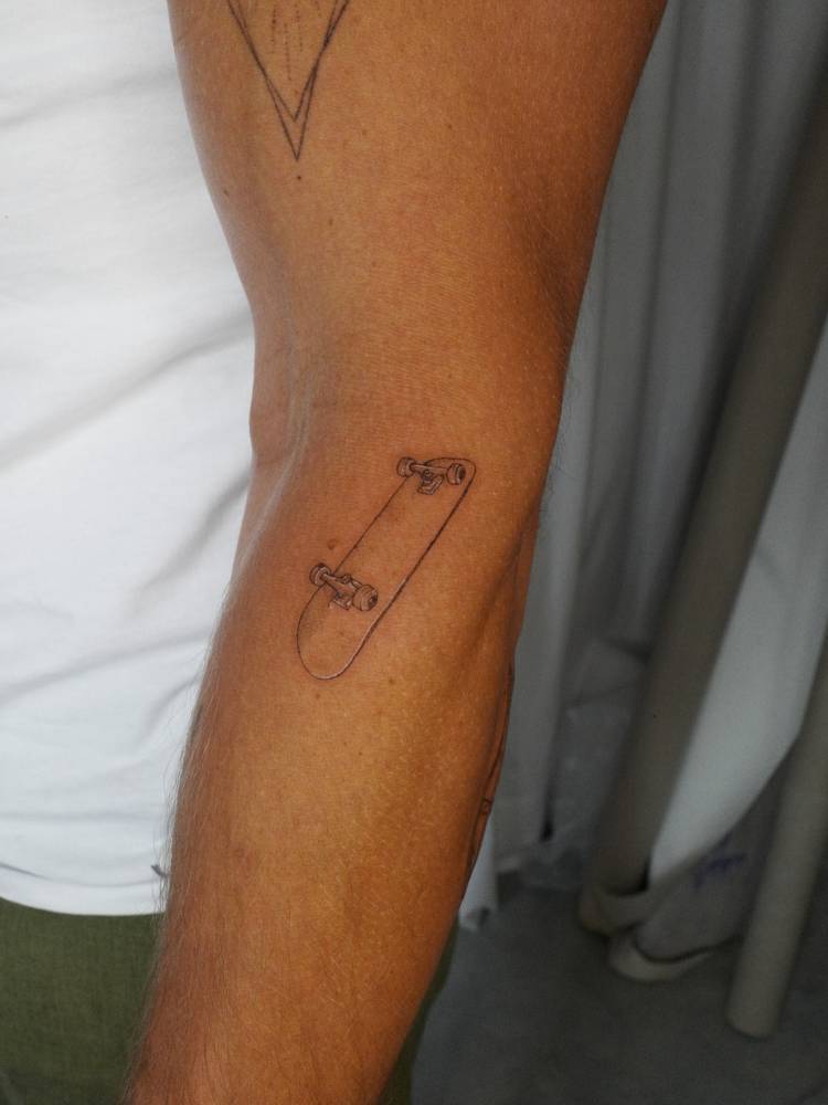 Skateboard tattooed pm the forearm, illustrative style.