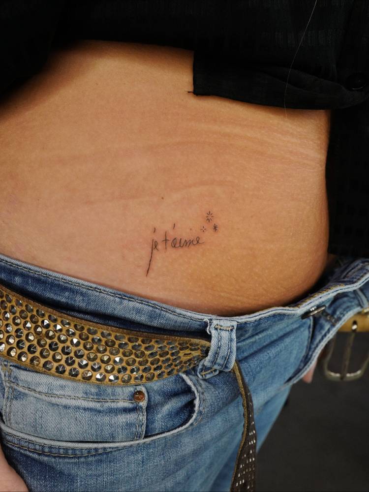 "Je t'aime" and sparkling stars tattoo located on the hip.