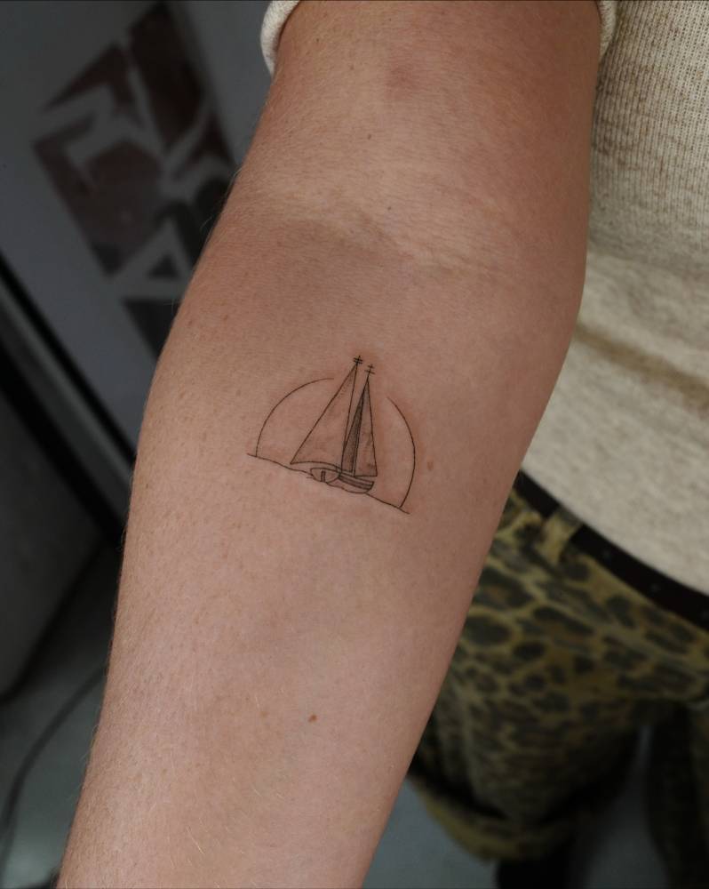 Illustrative style sailboat tattoo located on the inner forearm.