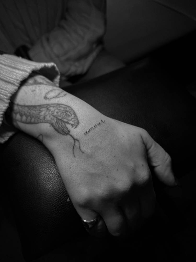 Handwritten font word "amour" tattooed on the wrist.