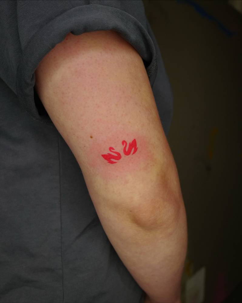 Red swans tattoo located on the tricep, minimalistic style.