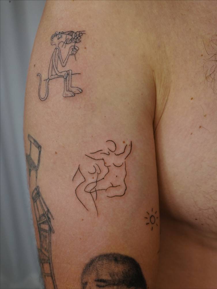 Nude women tattooed on the upper arm, done in fine line style.