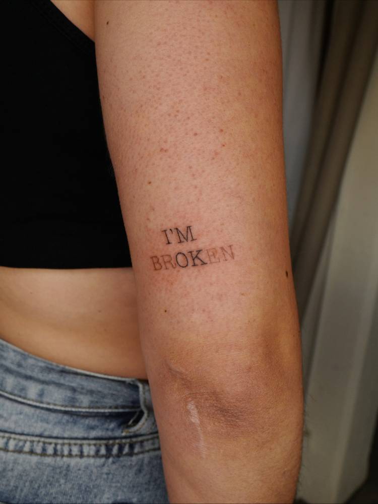 "I'm brOKen" lettering tattoo in typewriter font located on the tricep.
