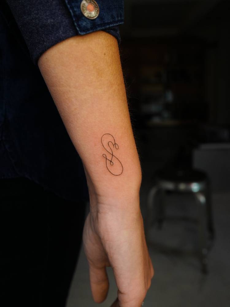 Infinity symbol and initials tattoo located on the wrist.