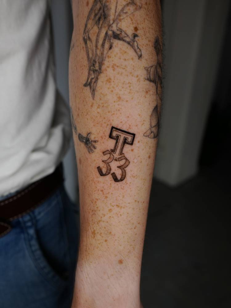 Letter "T" and number "33" tattoo located on the forearm.