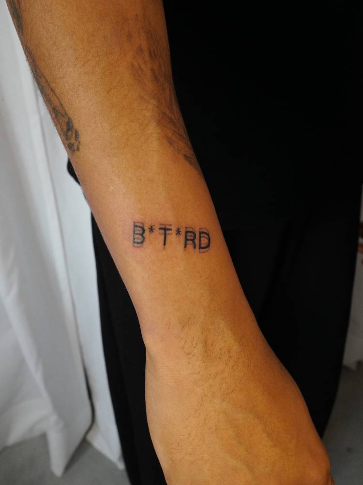 Blurry effect word "bâtard" tattooed on the wrist.