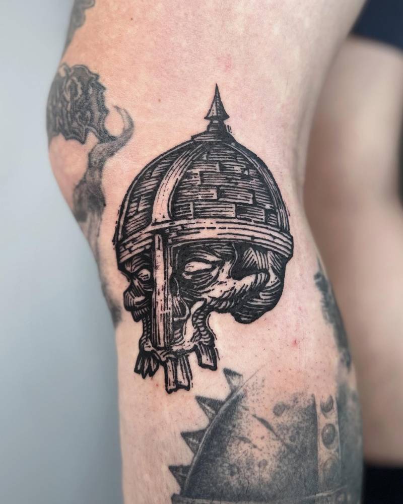 Engraving style skull and helmet tattoo located on the knee.
