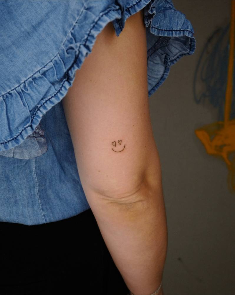 Smiley face tattoo located on the tricep, minimalistic style.