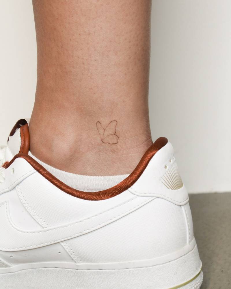 Minimalistic butterfly tattoo in fine line style located on the ankle.