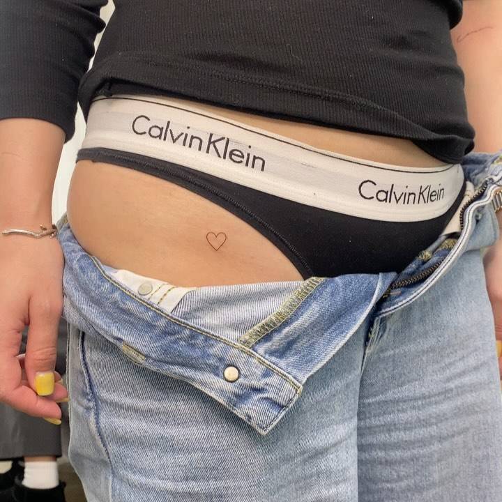 Minimalistic style heart tattoo located on the pelvis.