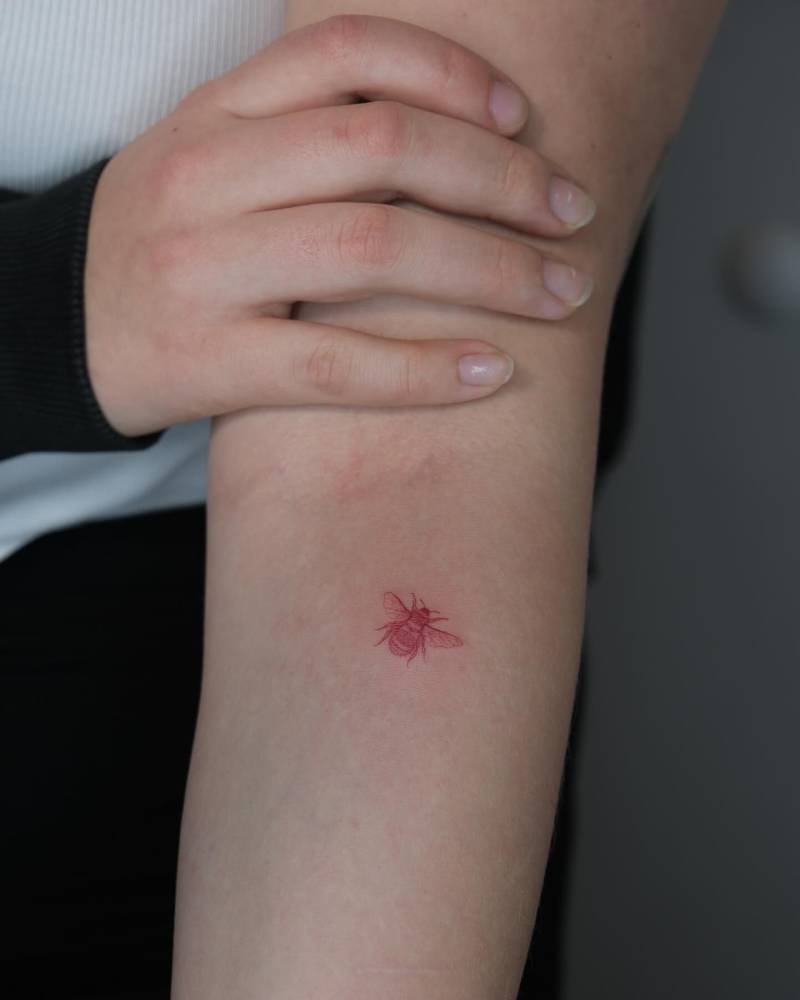 Tiny red bee tattoo located on the inner forearm.