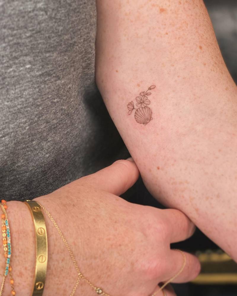 Fine line style scallop shell and flowers tattooed on the inner arm.